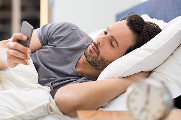 Un uomo giace a letto e guarda il telefono, apparentemente in attesa di un lungo messaggio di preghiera del buongiorno.