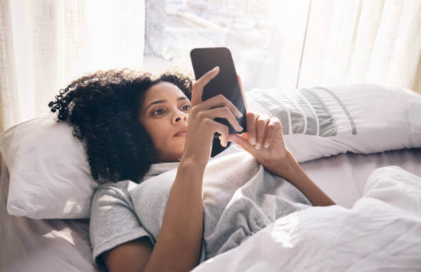 Una ragazza sdraiata sul letto guarda il suo telefono