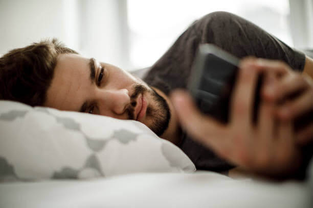 Un uomo sdraiato che guarda il suo telefono, con un'aria un po' triste