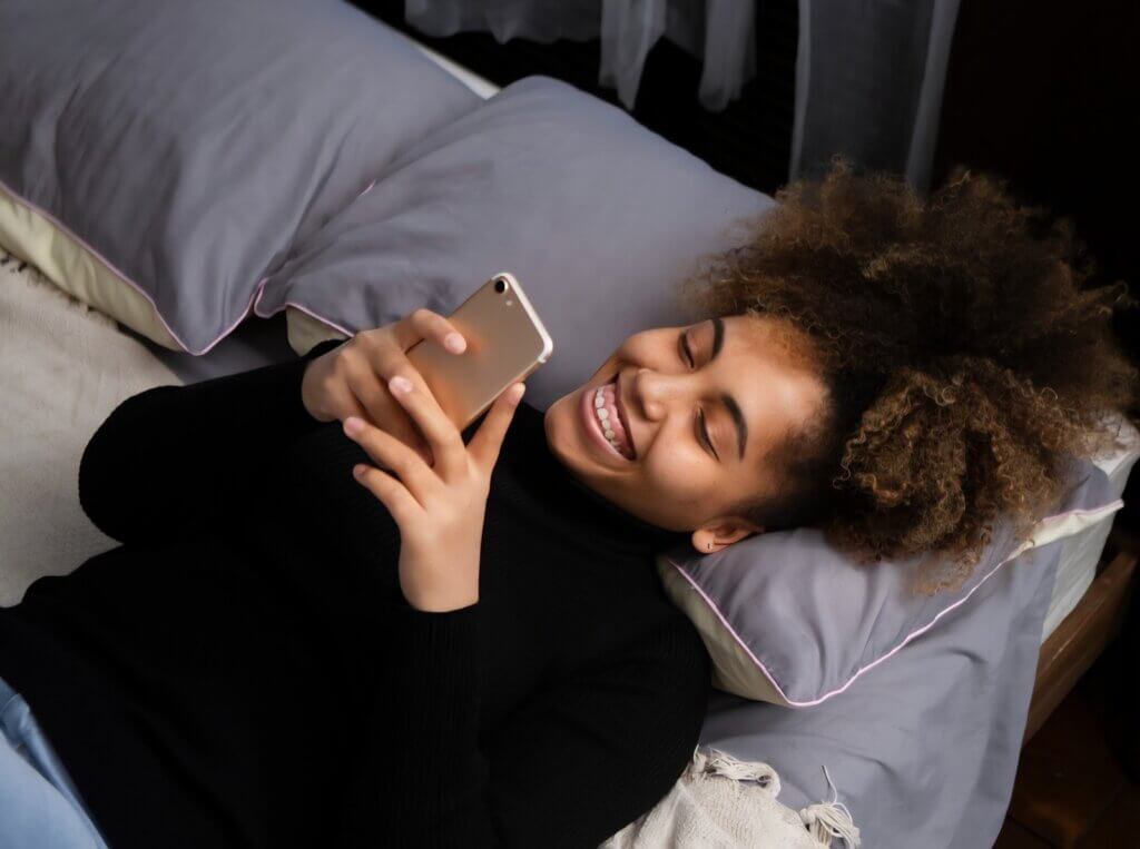 A woman lying in bed smiles after receiving Love Texts